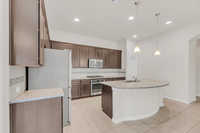 kitchen featuring light tile patterned flooring, appliances with stainless steel finishes, a sink, decorative light fixtures, and tasteful backsplash
