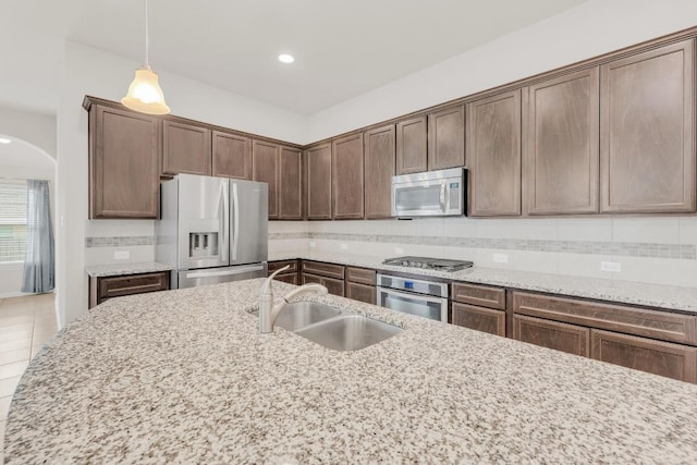 kitchen with decorative light fixtures, arched walkways, tasteful backsplash, a sink, and stainless steel appliances