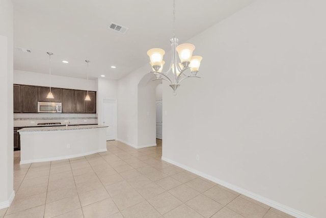 kitchen with backsplash, visible vents, arched walkways, dark brown cabinets, and stainless steel microwave