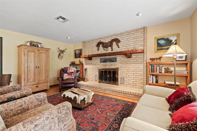 living room with a brick fireplace, visible vents, and wood finished floors