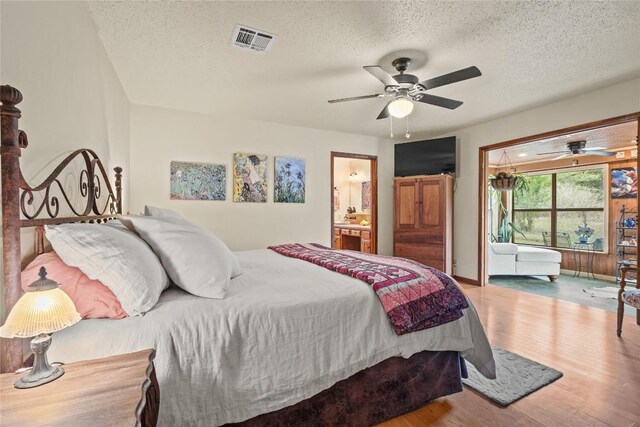 bedroom featuring ensuite bath, a textured ceiling, a ceiling fan, wood finished floors, and visible vents