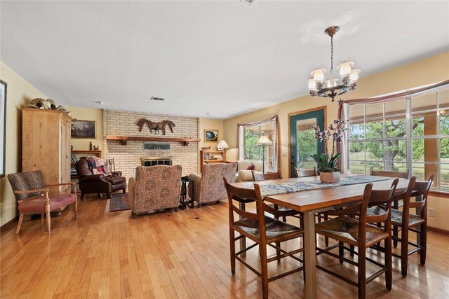 dining room featuring light wood-type flooring, a brick fireplace, visible vents, and an inviting chandelier
