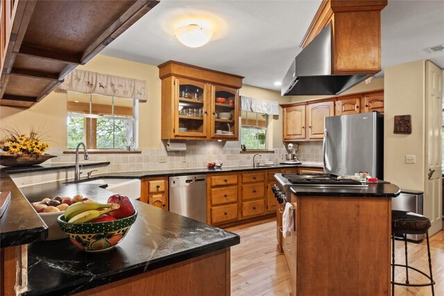 kitchen with a sink, a wealth of natural light, wall chimney range hood, and stainless steel appliances