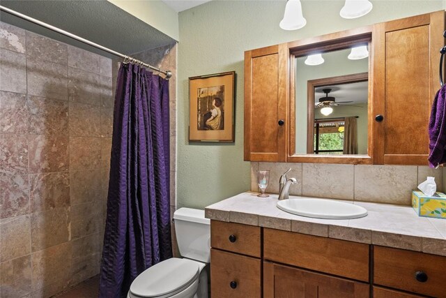 full bathroom with vanity, a textured wall, a tile shower, and toilet