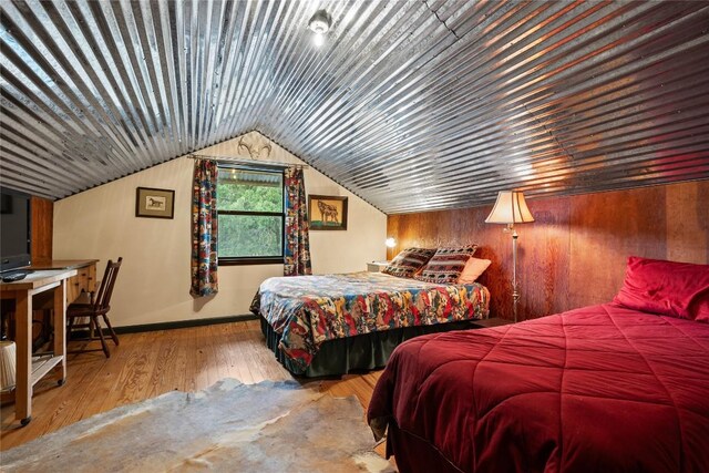 bedroom with wood finished floors, baseboards, lofted ceiling, and wooden walls