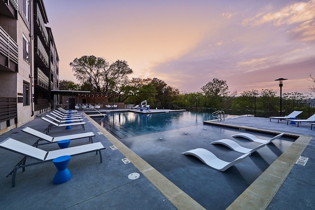 pool at dusk featuring a community pool, a patio, and fence