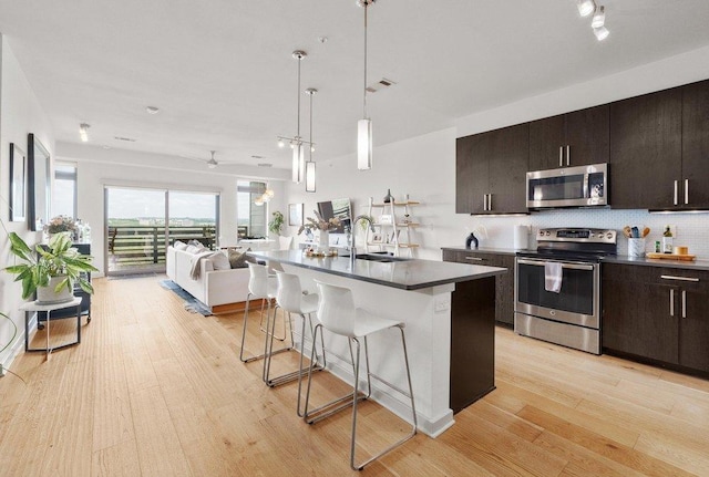kitchen with a kitchen bar, appliances with stainless steel finishes, light wood-type flooring, a sink, and open floor plan