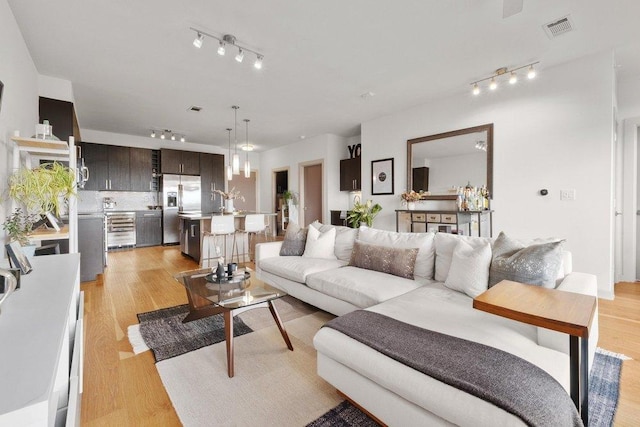 living room with light wood-style floors, track lighting, beverage cooler, and visible vents