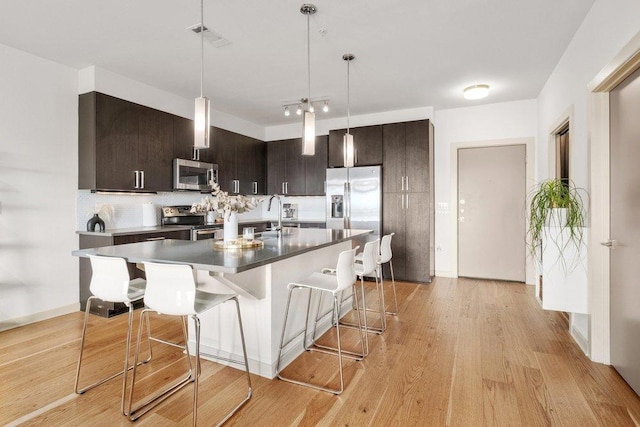 kitchen featuring appliances with stainless steel finishes, hanging light fixtures, tasteful backsplash, dark brown cabinets, and a breakfast bar