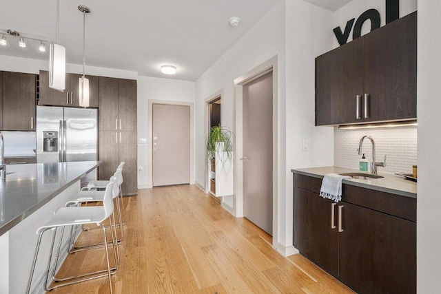 kitchen featuring decorative backsplash, dark brown cabinets, stainless steel fridge, and a sink