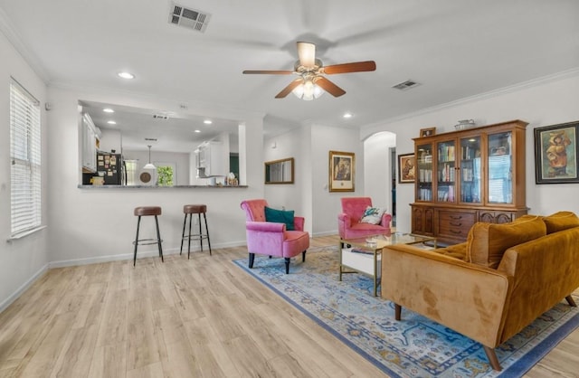 sitting room with visible vents, arched walkways, light wood finished floors, and ornamental molding
