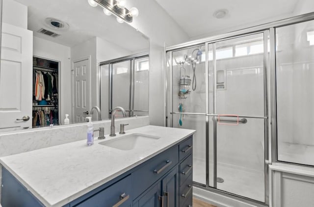full bathroom featuring vanity, a walk in closet, a stall shower, and visible vents