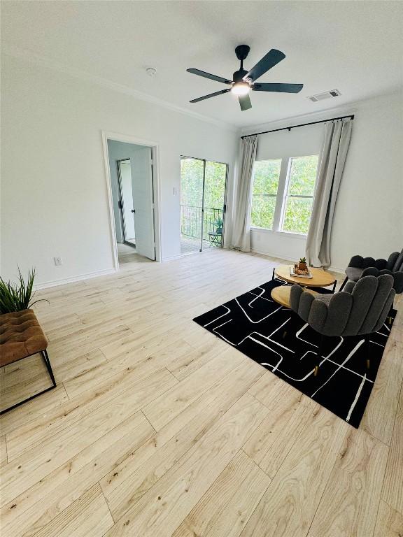 living room with a ceiling fan, visible vents, crown molding, baseboards, and wood-type flooring