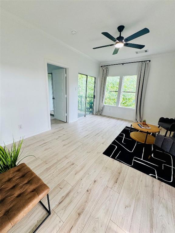 living room featuring a ceiling fan, visible vents, baseboards, ornamental molding, and light wood-style flooring