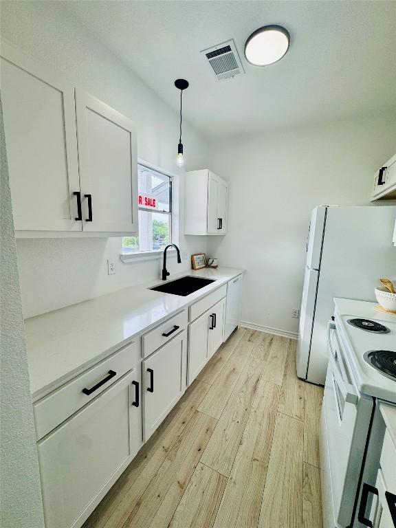 kitchen with visible vents, white appliances, light wood-type flooring, white cabinets, and a sink