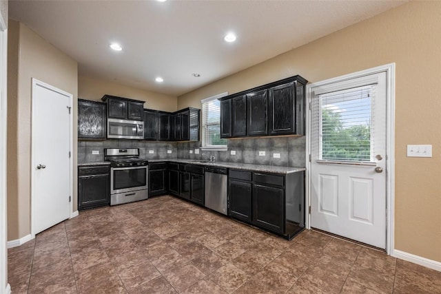349 Eagle Brook Ln, Buda, TX 78610 - kitchen featuring stainless steel appliances, dark cabinets, a sink, decorative backsplash, and baseboards