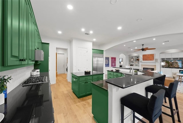 7921 W Rim Dr, Austin, TX 78731 - kitchen featuring green cabinets, a spacious island, arched walkways, stainless steel appliances, and light wood-style floors