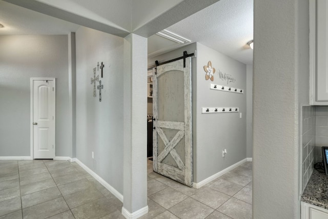 hallway with a textured ceiling, baseboards, a barn door, and light tile patterned floors