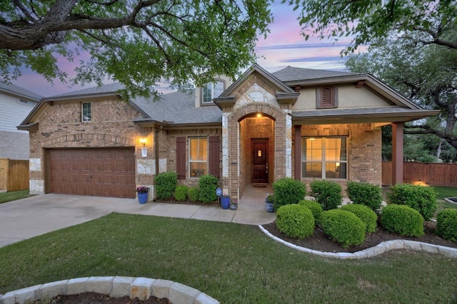 view of front of property featuring a front yard, roof with shingles, brick siding, fence, and concrete driveway