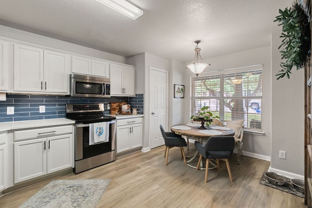 kitchen featuring white cabinets, appliances with stainless steel finishes, light wood-style floors, light countertops, and decorative backsplash