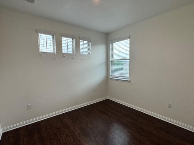 spare room featuring dark wood-style flooring and baseboards