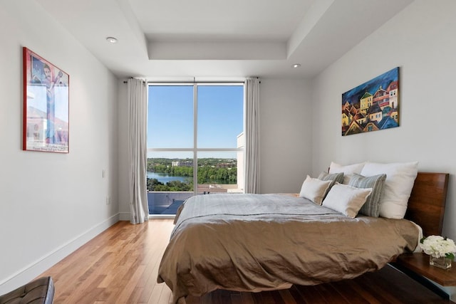 bedroom featuring recessed lighting, baseboards, a tray ceiling, and light wood finished floors