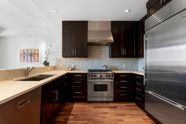 kitchen featuring decorative backsplash, high end appliances, a sink, light countertops, and wall chimney exhaust hood