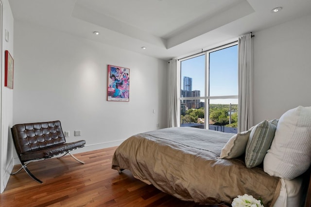 bedroom featuring baseboards, recessed lighting, a raised ceiling, and wood finished floors