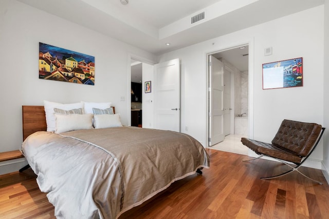 bedroom with baseboards, visible vents, wood finished floors, and ensuite bath