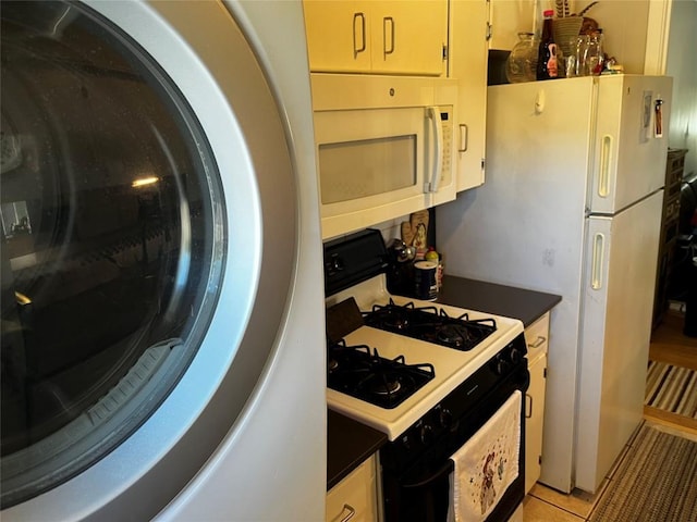 kitchen featuring dark countertops, washer / clothes dryer, light tile patterned floors, white microwave, and range with gas cooktop