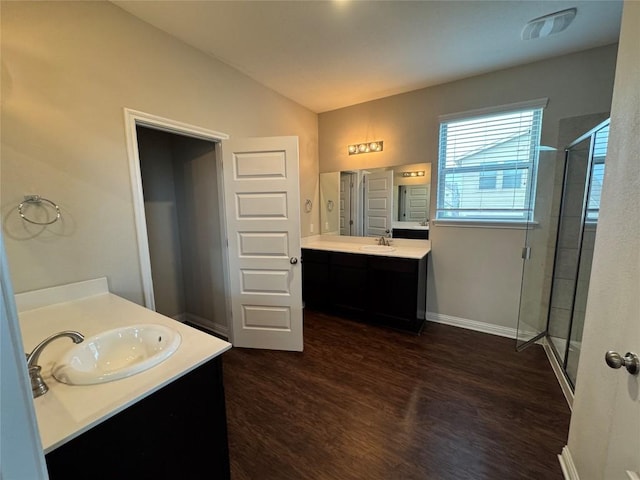 full bath with a stall shower, two vanities, a sink, and wood finished floors
