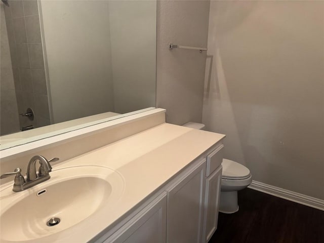 bathroom featuring vanity, toilet, baseboards, wood finished floors, and a shower