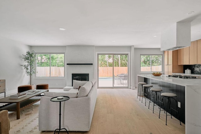 living area with recessed lighting, a glass covered fireplace, and light wood-style floors
