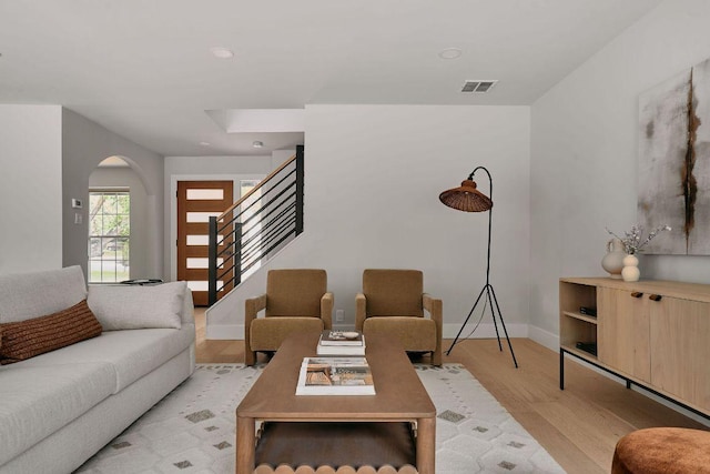 living room featuring light wood-style floors, arched walkways, baseboards, visible vents, and stairway