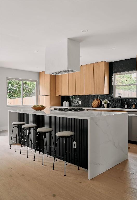 kitchen with stainless steel dishwasher, wall chimney exhaust hood, gas stovetop, tasteful backsplash, and light wood finished floors
