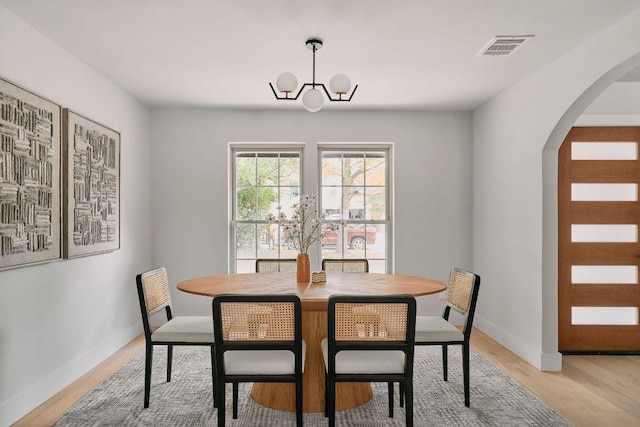 dining space featuring light wood-style floors, arched walkways, an inviting chandelier, and baseboards