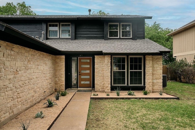 exterior space with a lawn, central AC unit, a shingled roof, and stone siding