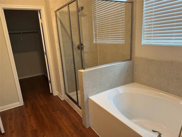 bathroom featuring wood finished floors, a bath, a walk in closet, and a stall shower
