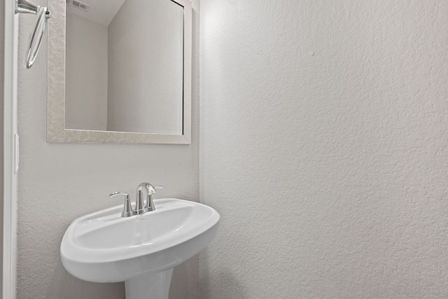 bathroom with a textured wall, visible vents, and a sink
