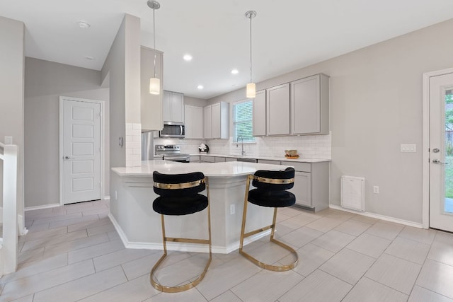 kitchen featuring backsplash, a kitchen bar, light countertops, a peninsula, and stainless steel appliances