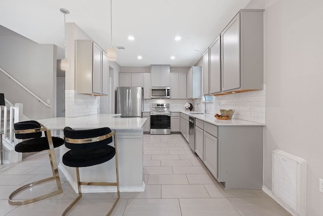 kitchen featuring appliances with stainless steel finishes, a sink, light countertops, gray cabinets, and a peninsula