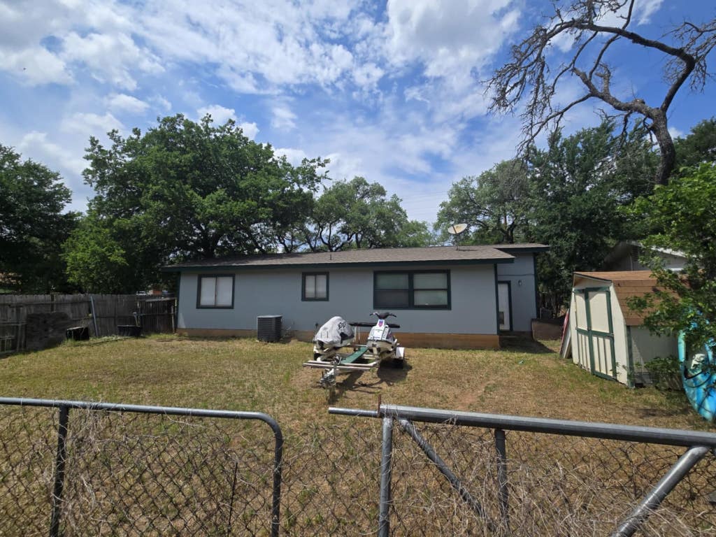 back of property featuring central AC, a storage shed, a fenced backyard, an outdoor structure, and a yard