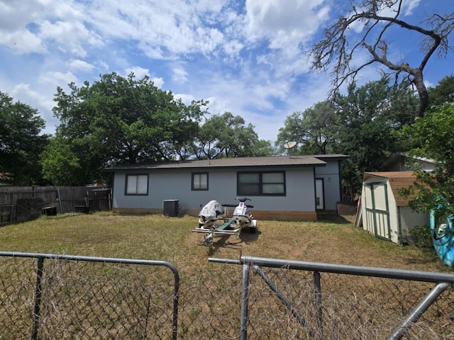 back of property featuring central AC, a storage shed, a fenced backyard, an outdoor structure, and a yard