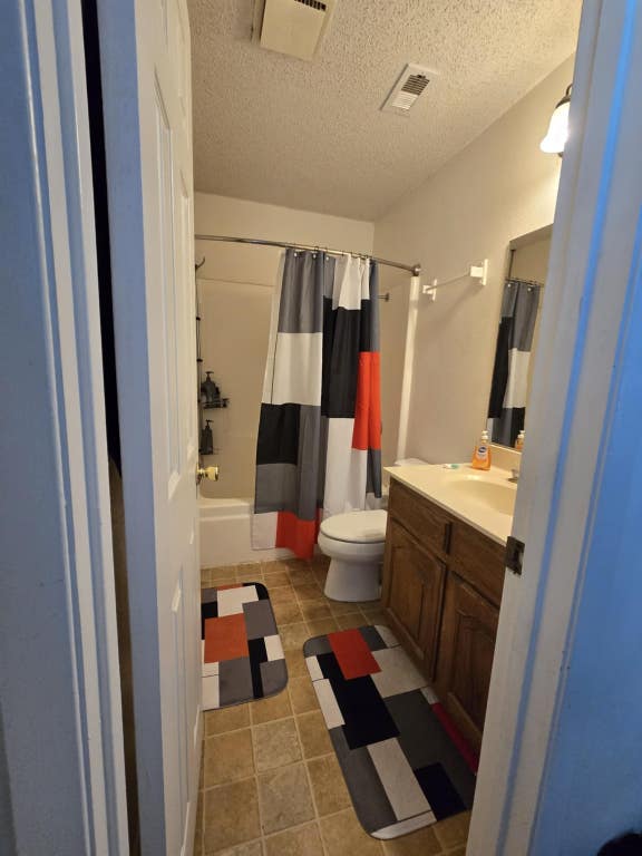 18215 Center St, Jonestown, TX 78645 - bathroom with tile patterned flooring, vanity, toilet, a textured ceiling, and shower / bathtub combination with curtain