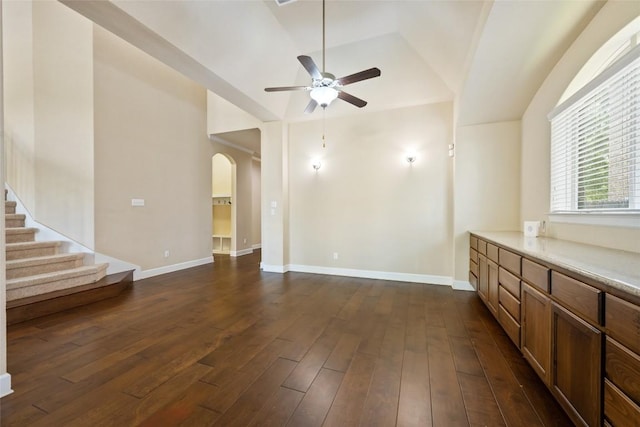 unfurnished living room featuring dark wood-style flooring, arched walkways, a ceiling fan, baseboards, and lofted ceiling