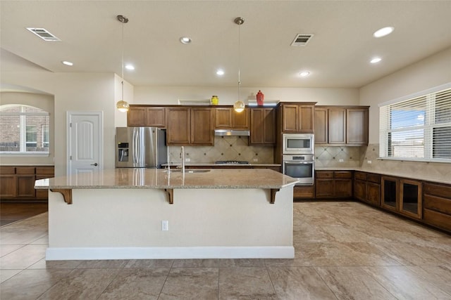 kitchen featuring visible vents, under cabinet range hood, a large island with sink, a sink, and stainless steel appliances