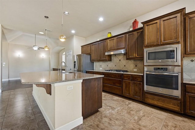 kitchen featuring decorative backsplash, a kitchen island with sink, appliances with stainless steel finishes, a sink, and under cabinet range hood