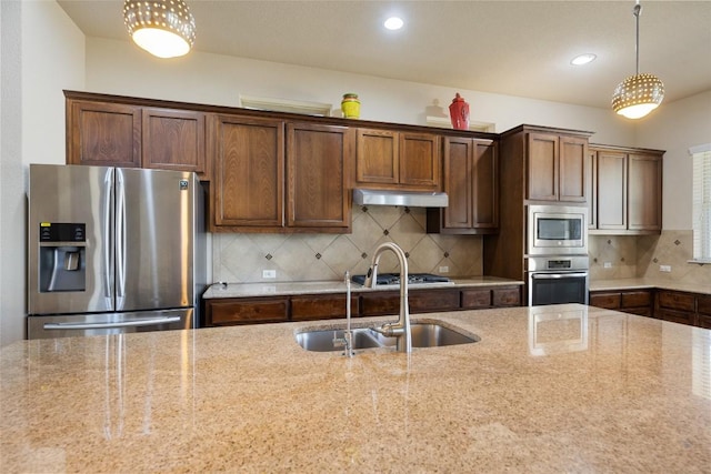 kitchen with light stone countertops, hanging light fixtures, a sink, stainless steel appliances, and under cabinet range hood