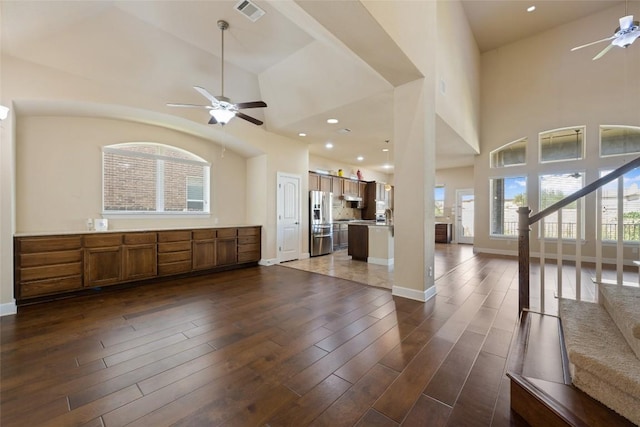 unfurnished living room featuring visible vents, a towering ceiling, baseboards, dark wood-style floors, and a ceiling fan
