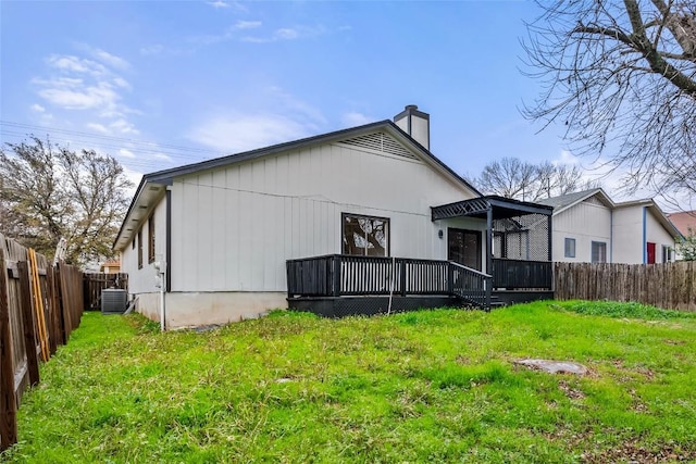 back of property with a chimney, a wooden deck, central air condition unit, a fenced backyard, and a yard